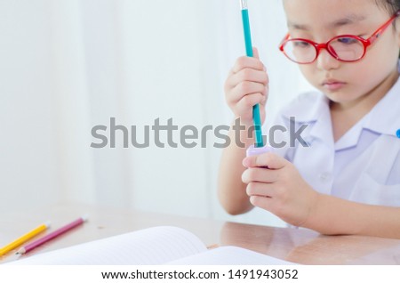 Cute asian girl White school uniform, blue skirt, wearing red glasses, sitting on homework after returning from school.Do not focus on objects.