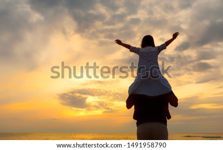 silhouette of little girl on dad's shoulders on the background of the setting sun on a seaside beach