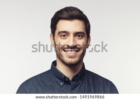 Close-up portrait of young smiling man in denim shirt isolated on gray background Royalty-Free Stock Photo #1491969866