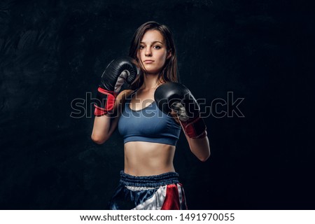 Portrait of serious female boxer in boxing gloves and sportive wear at dark photo studio.