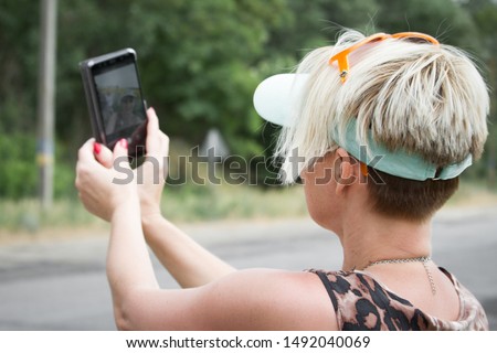 Adult blonde woman makes selfie on smartphone on a background of a field of sunflowers, selective focus