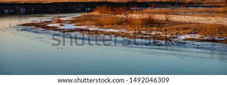 Water in the River and Shore with Dry Grass at Sunset. Winter Season, February. Web Banner. Natural Background.