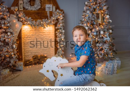 Boy rides a toy rocking horse, Christmas concept, fireplace and a toy tree in the background