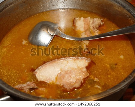 Stew in a pot with a ladle for pouring and cooked bacon