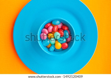Colored candies in blue plates and glasses on an orange background.