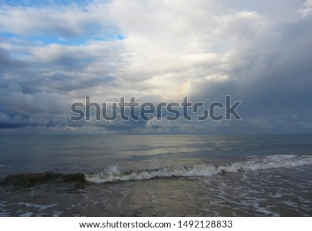 Among the rain clouds, a rainbow is visible above the sea.                               