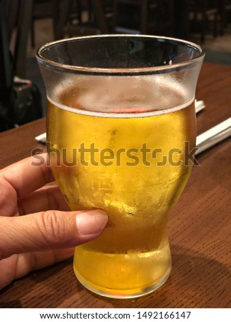 Close up of a cold glass of beer, with a hand holding it
