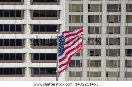 The american flag with business buildings on the background.