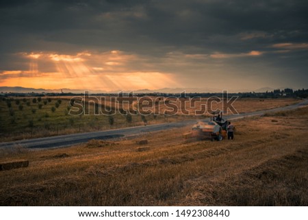 tractor makes straw bales in the agriculture field at harvest time and ray of the sunlight view