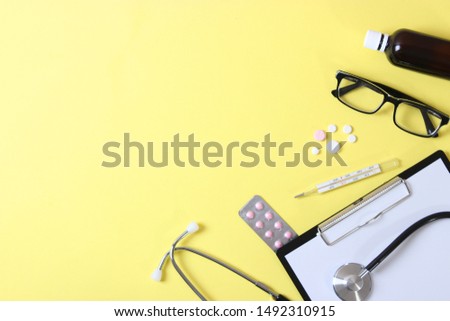 Doctor's desk top view. Stethoscope, pills, glasses and notebook on a colored background.
