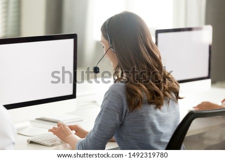 Call center operator in wireless headset with microphone using computer, looking at blank white screen mock up, busy female employee working in customer support service office, consulting client Royalty-Free Stock Photo #1492319780