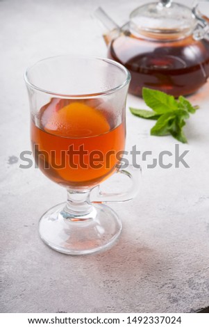 Transparent glass tea cup with teapot on a cement background