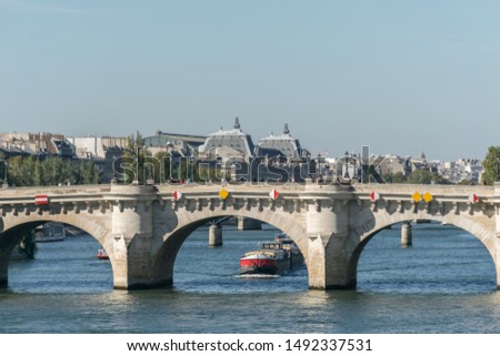 Overview of the architecture of a white bridge with yellow and red decorations over the Seine river in Paris with transportation boats passing by and an urban environment with trees in the background