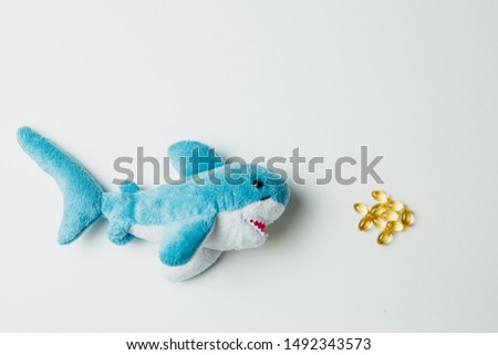 Toy shark swimming after scattered pills. Fish oil