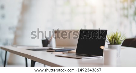 Open blank laptop in modern workplace with office supplies and decorations on white table 