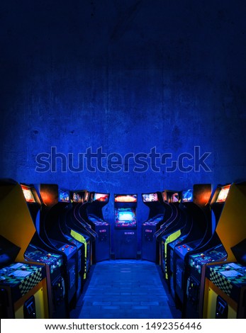 Old Unbranded Vintage Arcade Video Games in a dark gaming room with blue light with glowing displays and concrete wall - vertical photo of retro design with free copy space for a poster or magazine