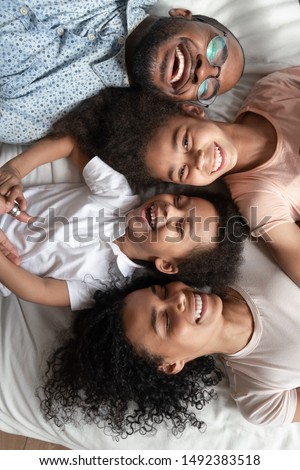 Close up vertical portrait view from top african couple small kids laughing lying down on bed, family stable relationships high degree of trust, connection protection happy family is happiness concept Royalty-Free Stock Photo #1492383518