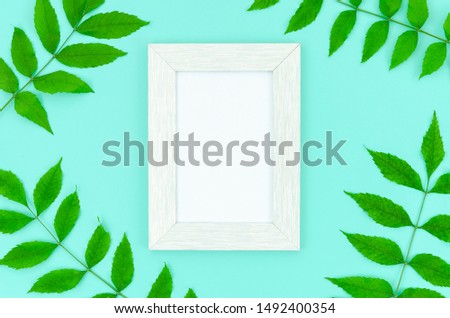 Flat lay frame from green leaves and white photoframe on a mint background. Mockup with copy space