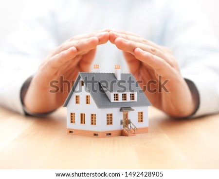 Protect your house concept. Small toy house covered by hands Royalty-Free Stock Photo #1492428905
