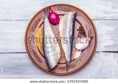 Traditional Norwegian slightly salted herring. Healthy seafood concept. Vegetarian ingredient with fresh onion, dry spice on ceramic plate. Rustic style, wooden boards background, copy space, top view