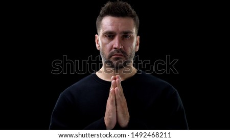 Crying male joining hands and praying on black background, sins atonement, faith