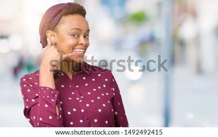 Beautiful young african american woman wearing head scarf over isolated background smiling doing phone gesture with hand and fingers like talking on the telephone. Communicating concepts.