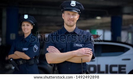 Kind police officers smiling standing near police station, ready to help, order Royalty-Free Stock Photo #1492492898