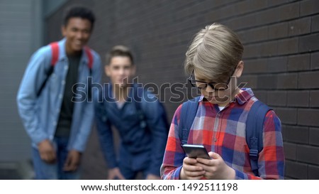 Junior student reading offensive post in phone, boys mock behind, cyberbullying Royalty-Free Stock Photo #1492511198