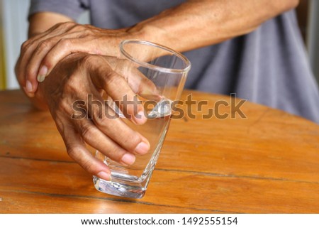 Elderly man is holding his hand while drinking water because Parkinson's disease.Tremor is most symptom and make a trouble for doing activities such as drinking.Health care or elderly concept. Royalty-Free Stock Photo #1492555154