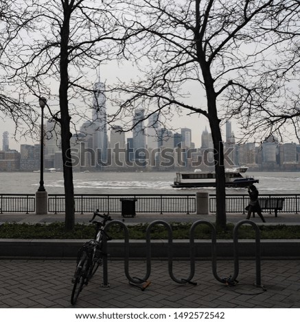 New York skyline behind tree silhouettes, boat cruising the river a bicycle secured to the bicycle rack and a person walking