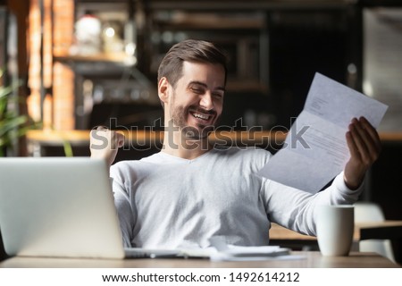Excited business man student reading postal mail letter overjoyed by great news, happy male winner holding paper bill with loan approval celebrate taxes refund receive salary rise payment sit at desk Royalty-Free Stock Photo #1492614212
