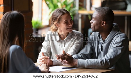 Smiling young mixed ethnicity couple talk decide on financial mortgage deal consider insurance loan meeting bank manager, female insurer consult interracial customers offer contract, business advice