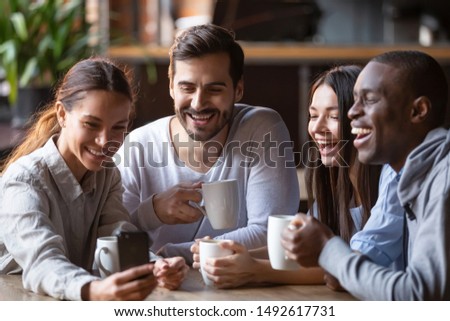 Happy diverse friends taking group selfie on cellphone in cafe, cheerful multiracial students making photo using snapshot app watching funny video on smartphone sitting at coffee shop table together