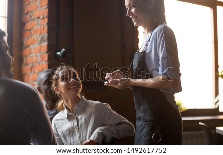 Happy female waitress holding notepad taking order serving clients in cafe pub restaurant, polite serving staff worker talking to guests diverse friends group choose food and drinks, customer service Royalty-Free Stock Photo #1492617752