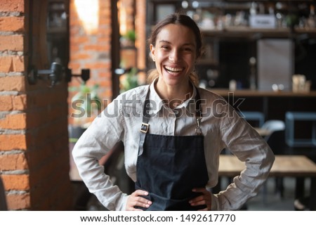Cheerful young waitress wearing apron laughing looking at camera, happy businesswoman small business owner of girl entrepreneur cafe employee posing in restaurant coffee shop interior, portrait Royalty-Free Stock Photo #1492617770