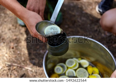 Close up photo of man's hand holding a cup and pouring lemonade in the forest