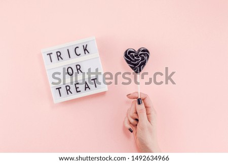 Creative Halloween Day composition flat lay top view holiday celebration sweet black lollipop heart hand lightbox pink paper background copy space Template greeting card design social media