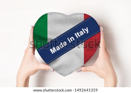 Inscription Made in Italy, the flag of Italy. Female hands holding a heart shaped box. White background.