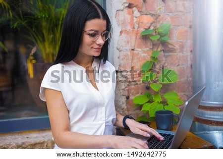Casual dressed woman skilled internet worker connected to public wifi via pc laptop computer while sitting in modern coffee shop outdoors. Female student in glasses online learning via notebook gadget