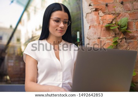 Stylish female in glasses skilled creative writer web pages checking e-mail on portable laptop computer while sitting in coffee shop during free time in weekend. Hipster girl using applications 