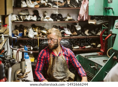 Shoemaker in his workshop. A man with a beard in a plaid shirt at work