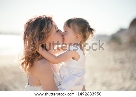 Mother and daughter hugging and kissing on the beach at sunset. Love and care concept. 