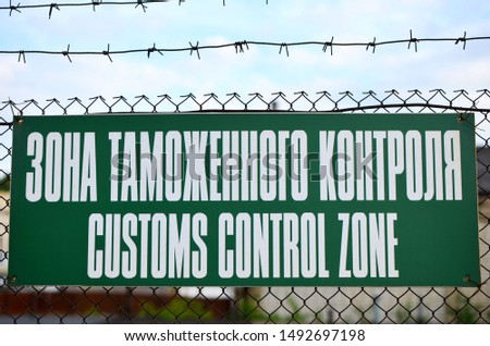 Green sign with an inscription in English: "Customs Control Zone" on the fence with metal barbed wire. Storage customs clearance. Translation from Russian: Customs Control Zone