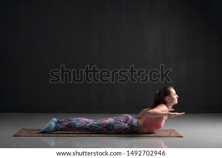 Sporty woman practicing yoga, doing Salabhasana pose variation. Studio shot