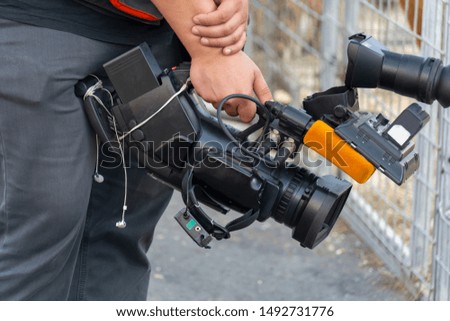 Video camera in the hands of a man close-up. The camera operator works with his equipment. Concept: reportage shooting, news, work of journalists.