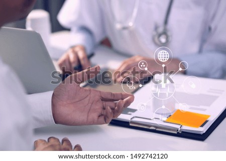 Female doctor at table with laptop and papers and showing pills in jar to a man patient sitting near. Medical technology networking concept.