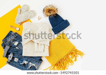 Blue winter hat with jeans, sweater, mittens and yellow scarf on white background. Women's stylish autumn or winter outfit. Trendy clothes collage. Flat lay, top view.