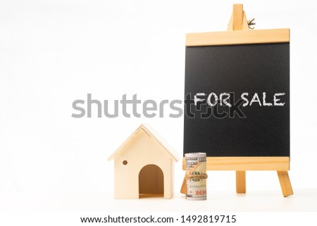 “FOR SALE” wordings on a chalkboard with rolled up money and miniature house