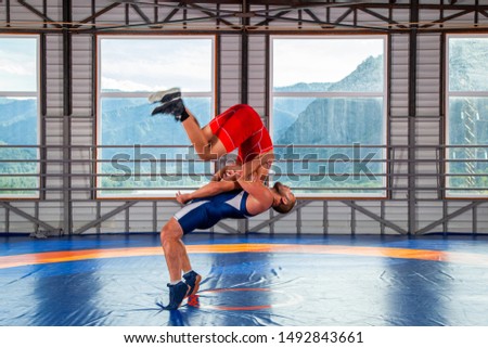 The concept of fair wrestling. Two greco-roman  wrestlers in red and blue uniform making a suplex wrestling  on a wrestling carpet in the gym.The concept of male wrestling and resistance