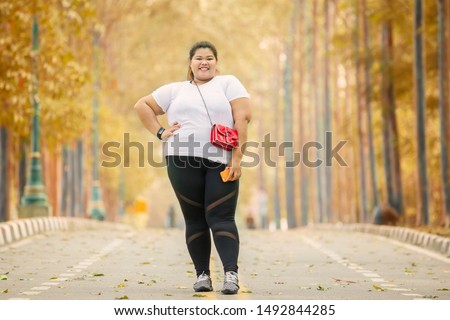 Picture of fat woman looks happy while posing on the road with autumn season background